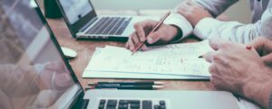 Duas pessoas realizando um planejamento utilizando dois notebooks e um papel com anotações.