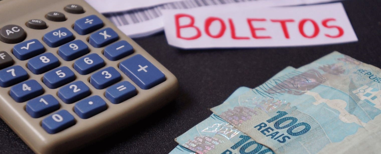 Uma calculadora, algumas notas de cem reais e um papel escrito "boletos" em uma mesa.